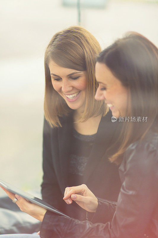 Two friends using digital tablet on bus station